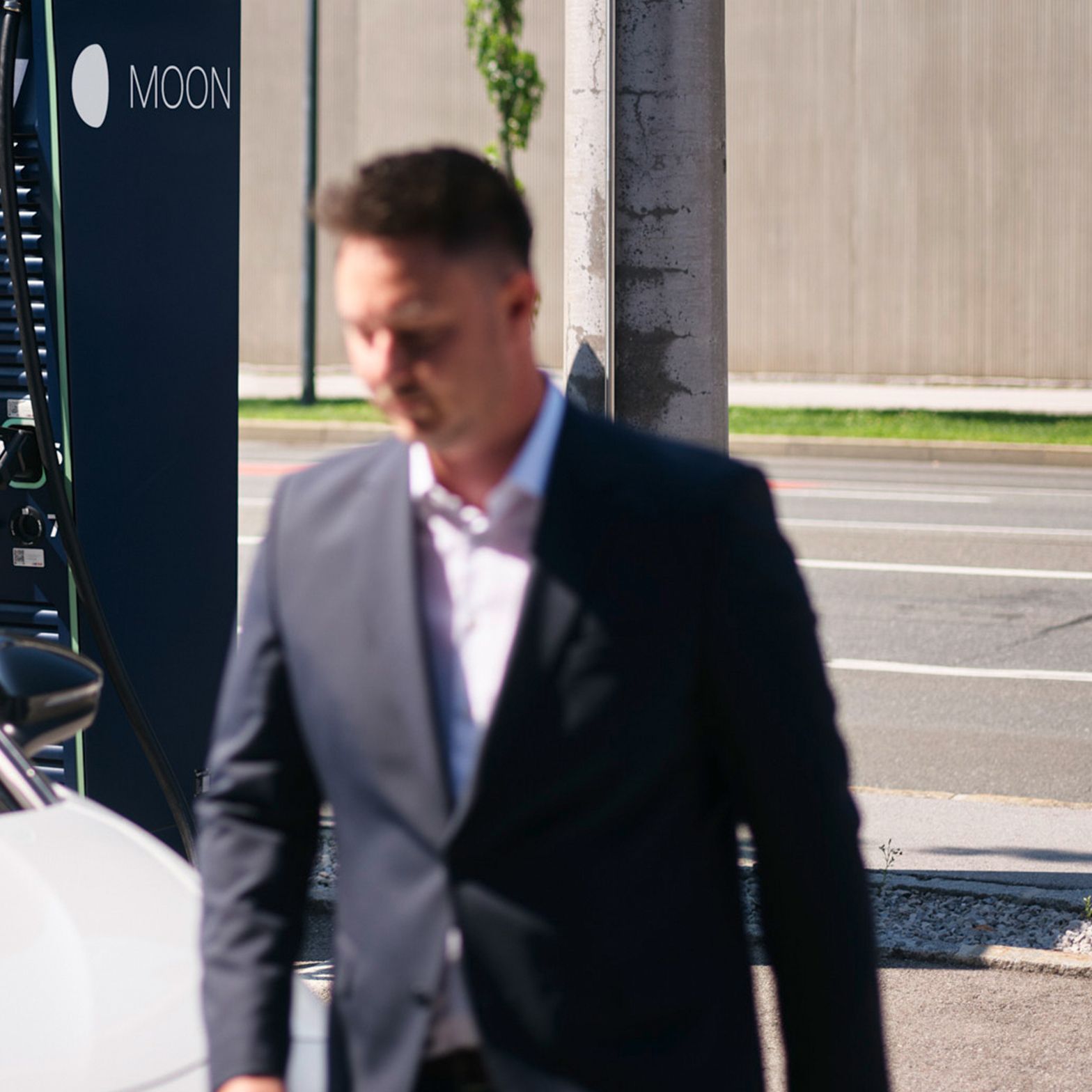 Moški hodi mimo električnega vozila pred hitro polnilno postajo.