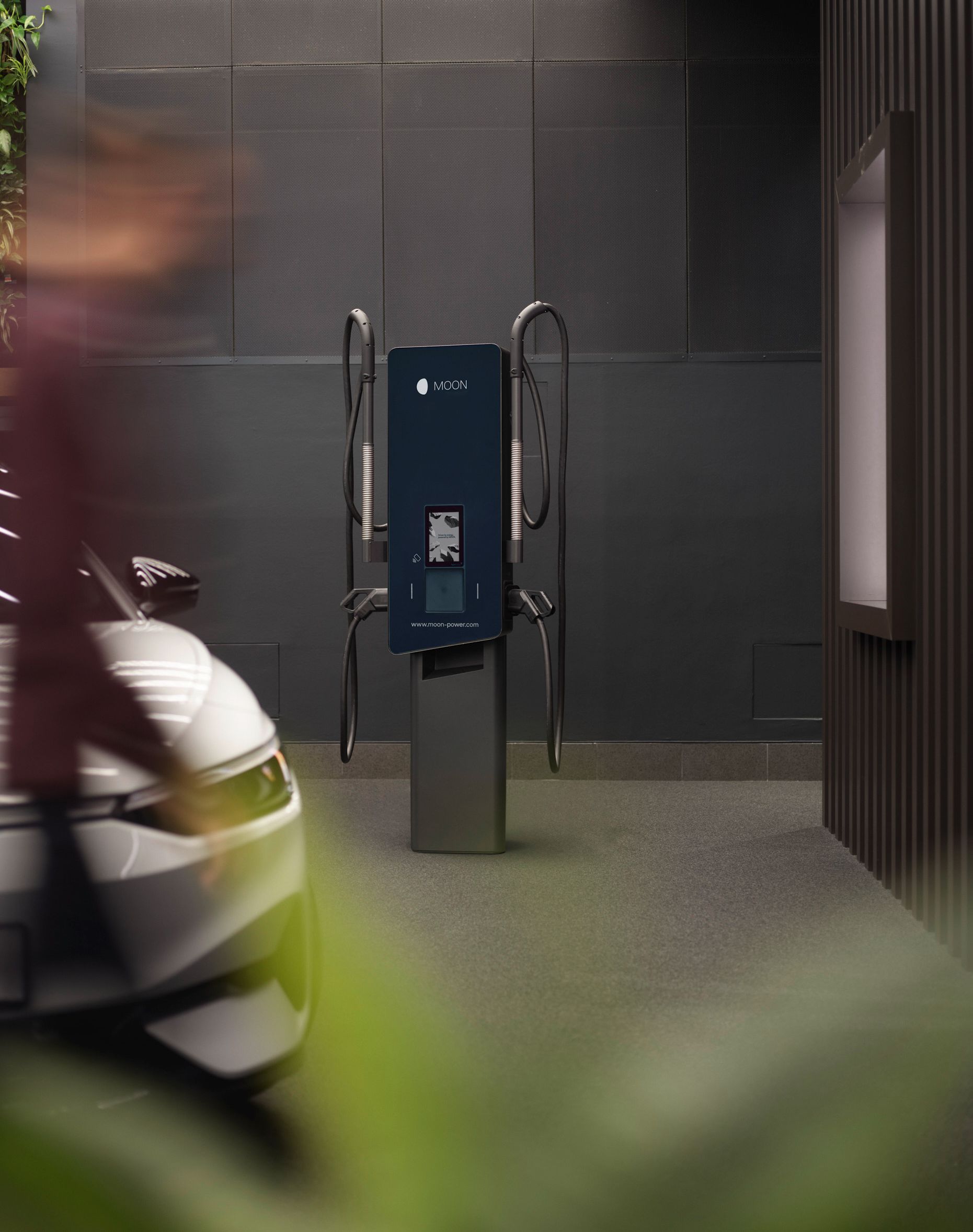 Stenska polnilna postaja pred sivo steno z električnim avtomobilom v ospredju