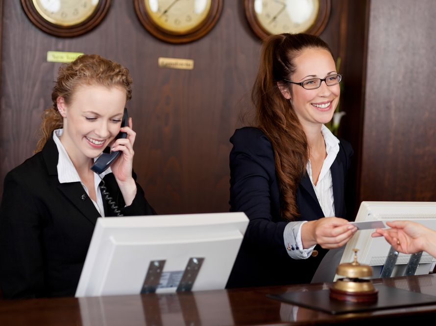 Recepcija hotela z dvema zaposlenima za pultom.