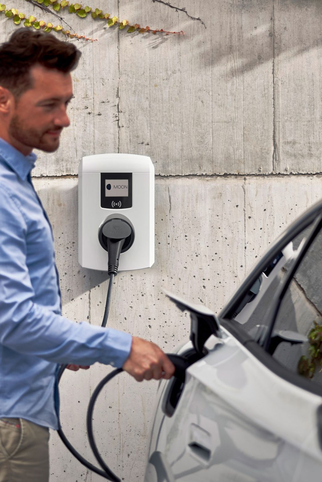 Moški pred stavbo priklaplja električni avto na stensko polnilnico.