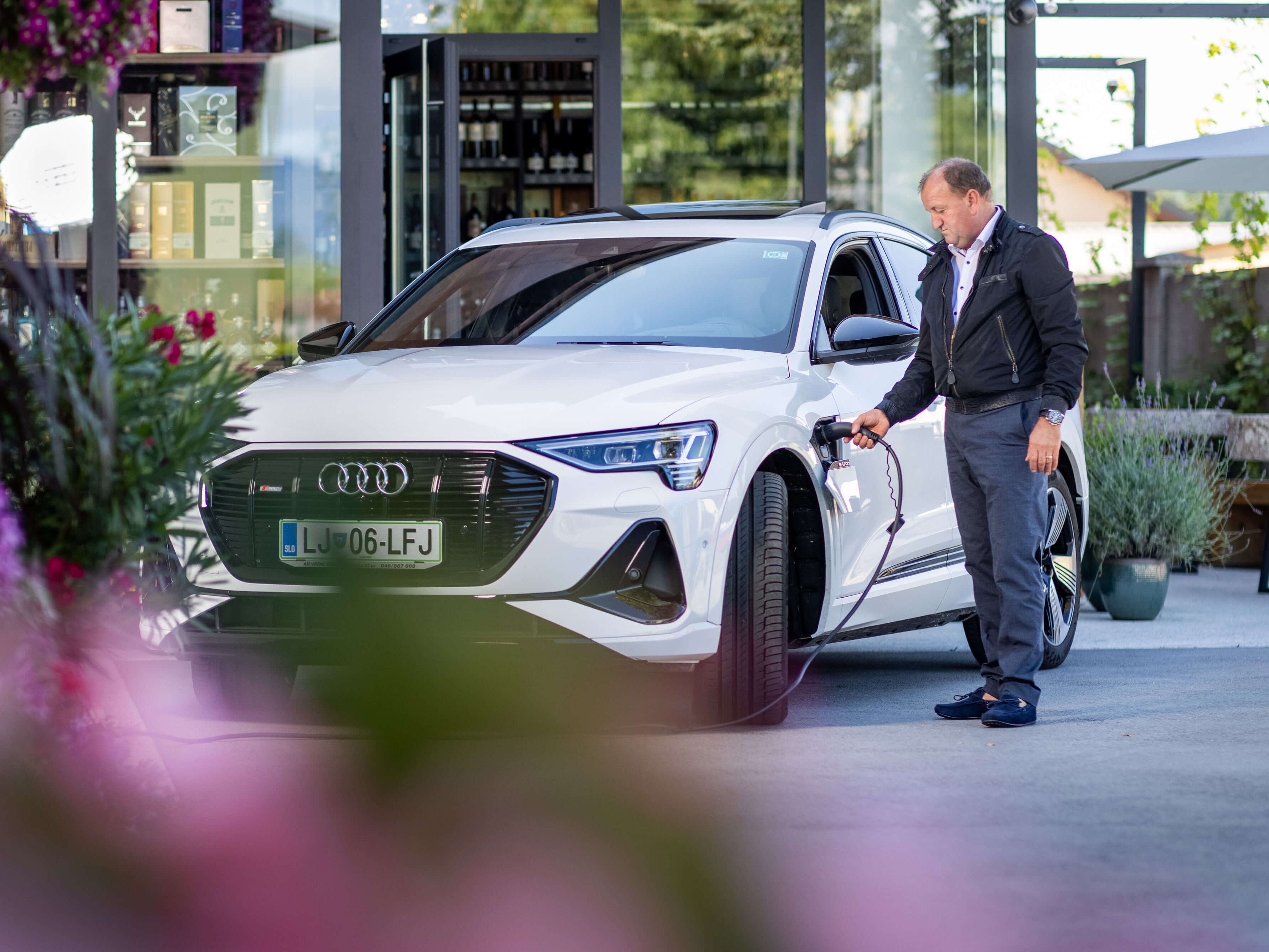 Moški pred stavbo priklaplja električni avto na polnilno postajo.