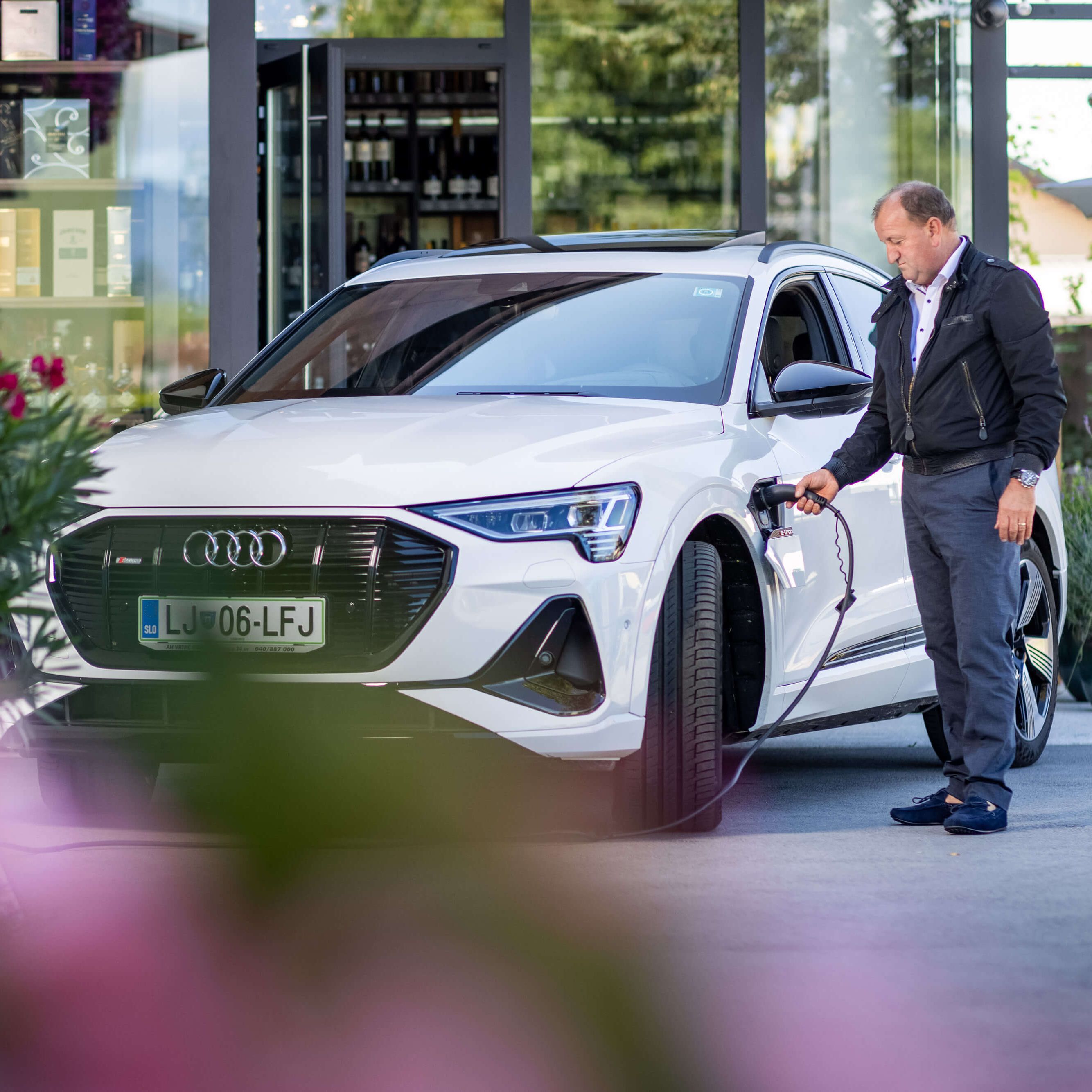 Moški pred stavbo priklaplja električni avto na polnilno postajo.