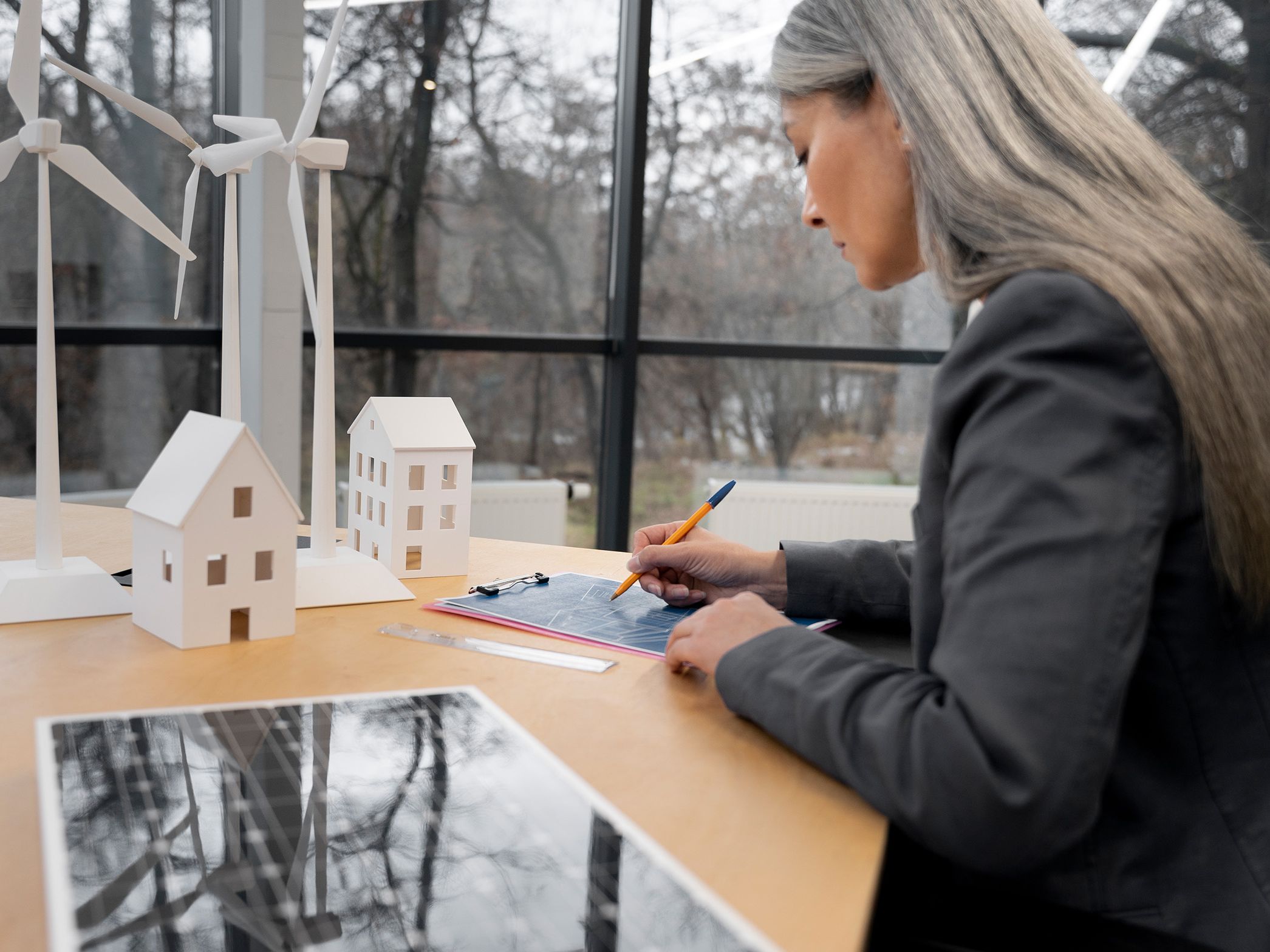 Ženska stoji ob mizi in si nekaj zapisuje, v svetlem in sodobnem interierju.