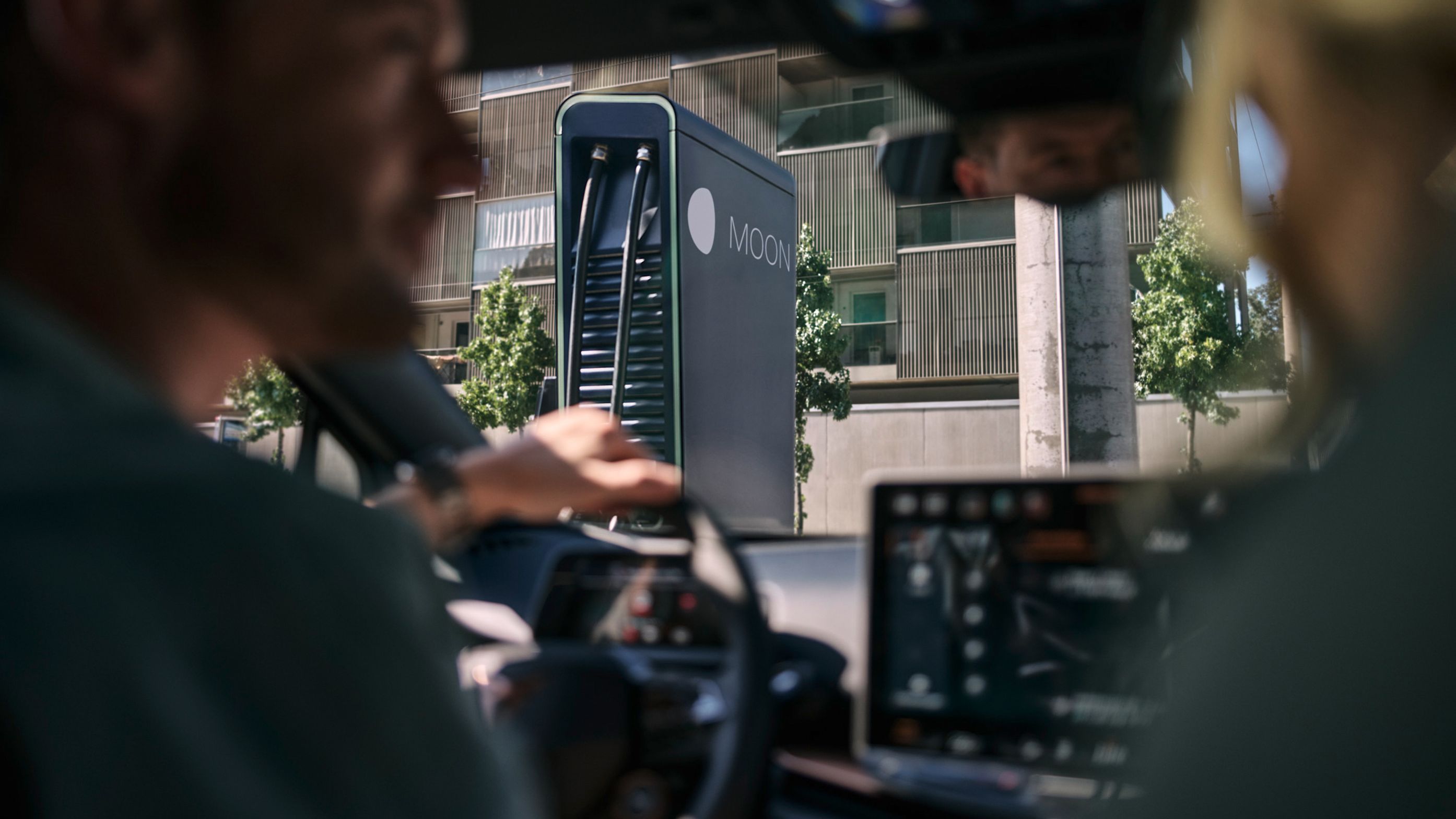 Dve osebi sedita v električnem vozilu pred hitro polnilno postajo.