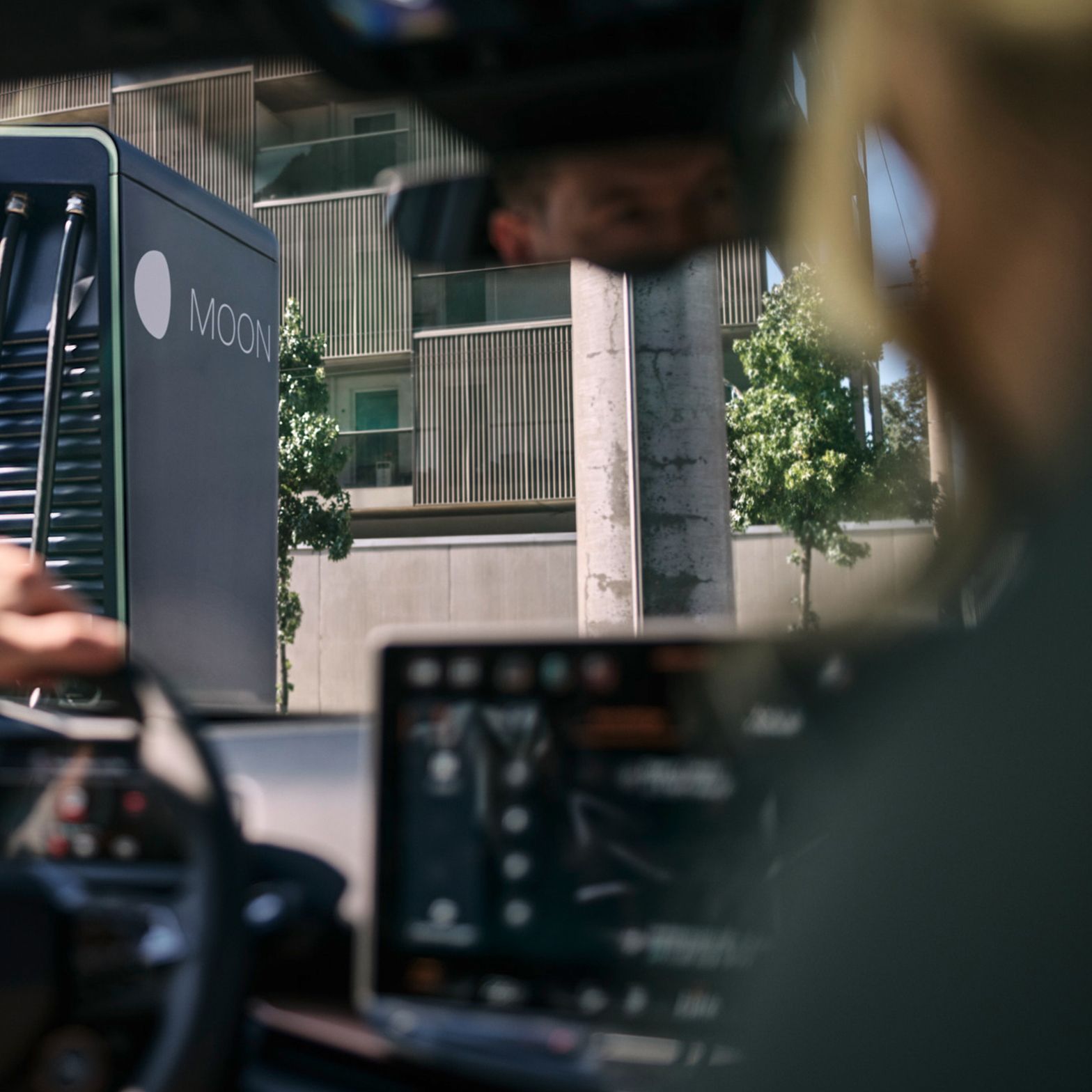 Dve osebi sedita v električnem vozilu pred hitro polnilno postajo.