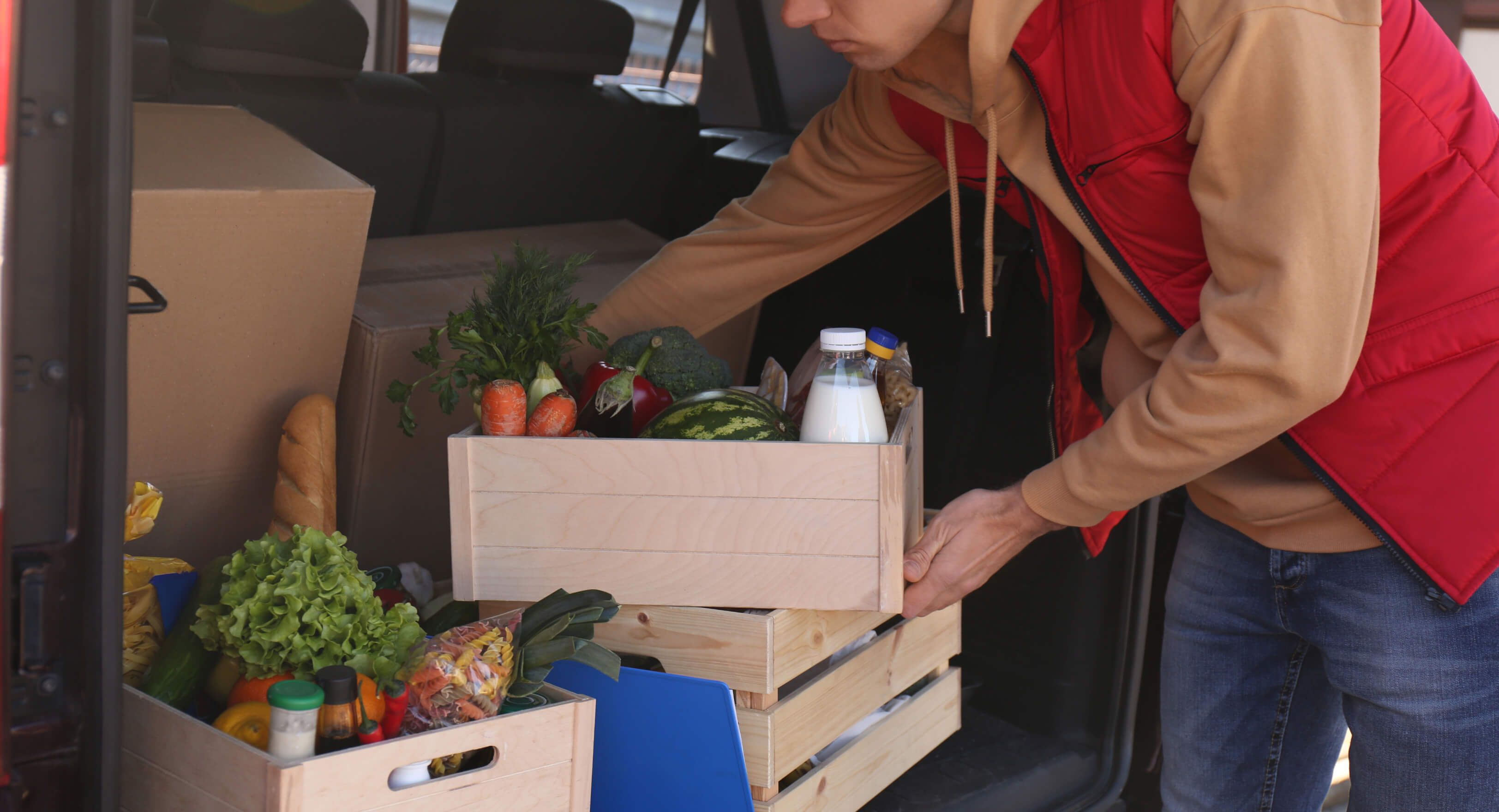 Dostavljavec jemlje hrano iz prtljažnika službenega vozila pred hotelom ali gostilno.