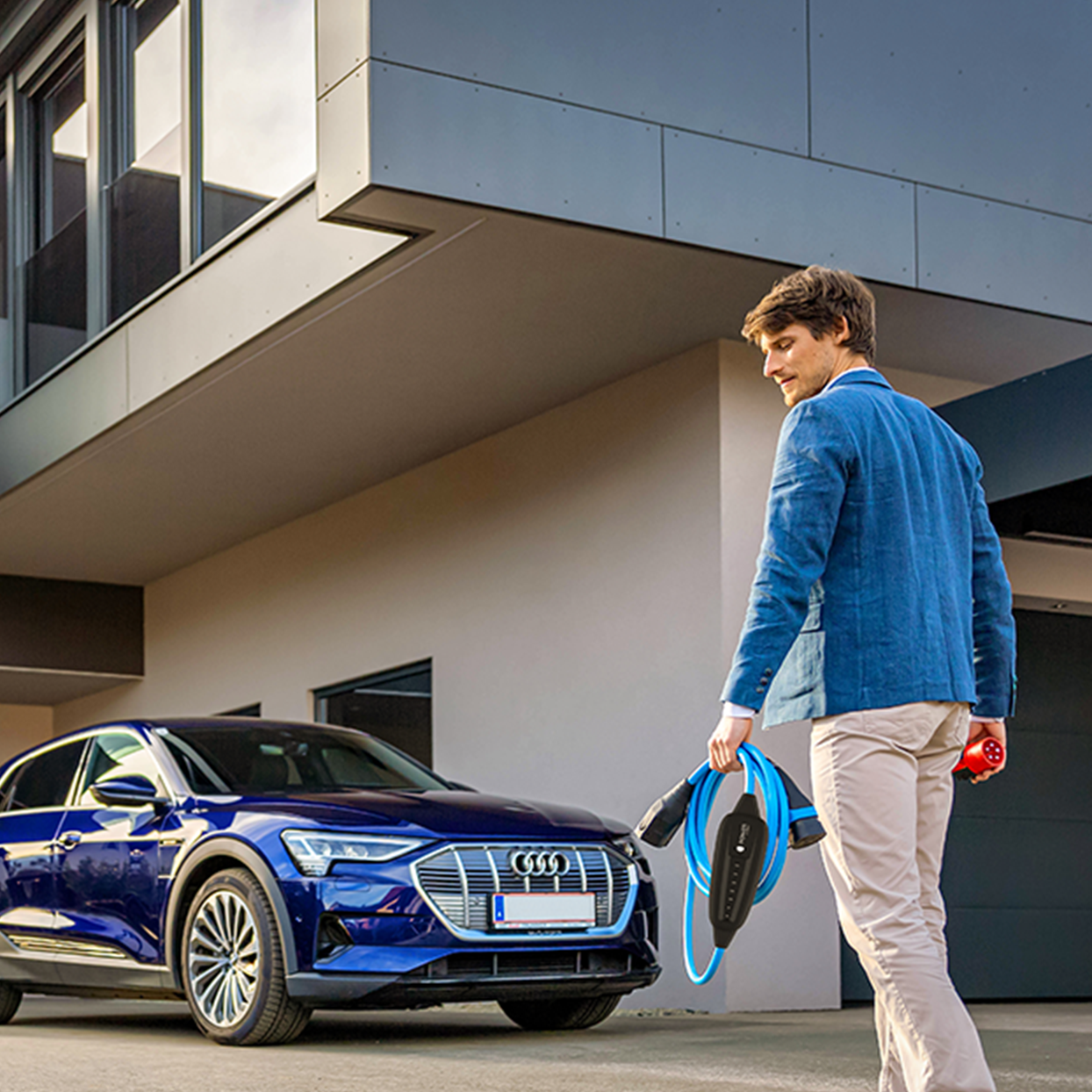 Oseba hodi proti električnemu avtomobilu s kablom v roki