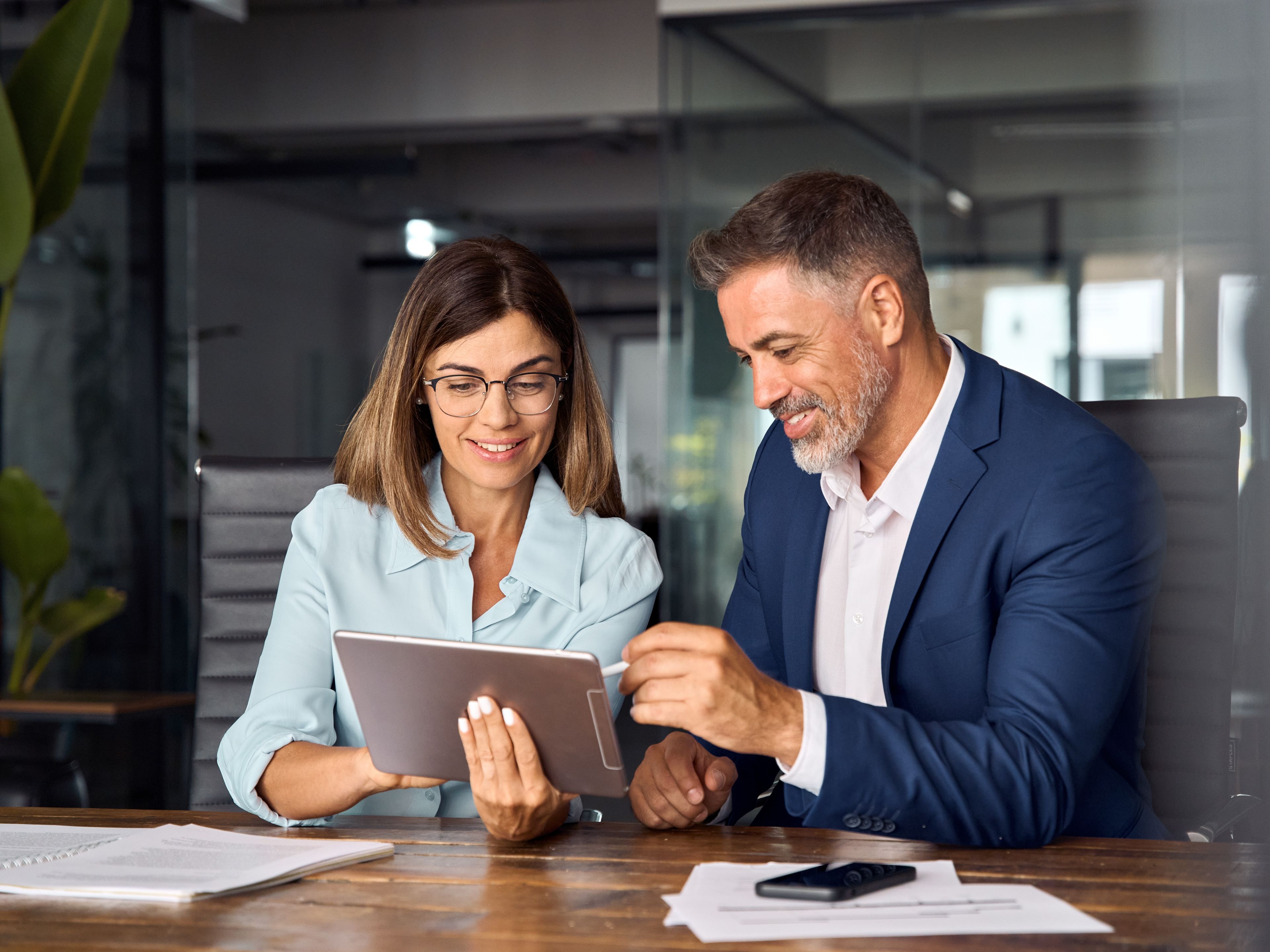 Moški in ženska na sestanku v pisarni, pri čemer ženska drži tablico, moški pa ji nanjo kaže z elektronskim pisalom.
