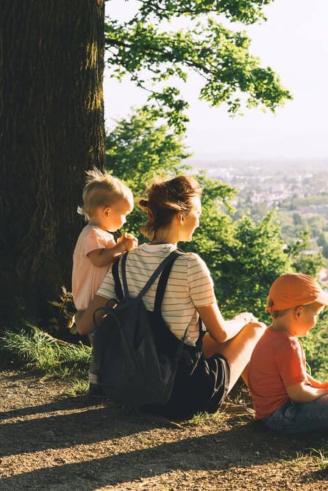 Mama z dvema majhnima otrokoma sedi na hribčku s pogledom na mesto.