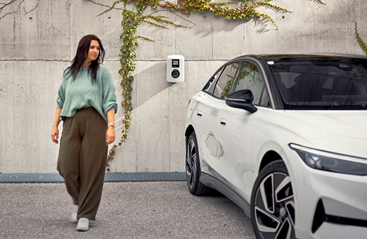 Ženska stoji ob avtomobilu pred MOON stensko polnilnico.